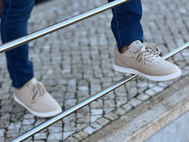 A man in blue jeans poses on a metal rail-guard with his beige hemp shoes.